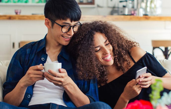 Un homme et une femme sur un canapé regardant un téléphone portable protégé par Norton 360 for Mobile.